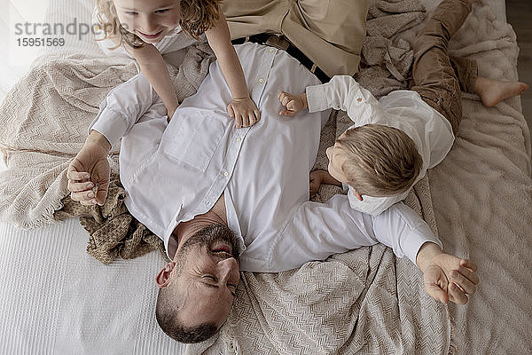 Vater liegt im Bett und spielt mit seinen beiden Kindern
