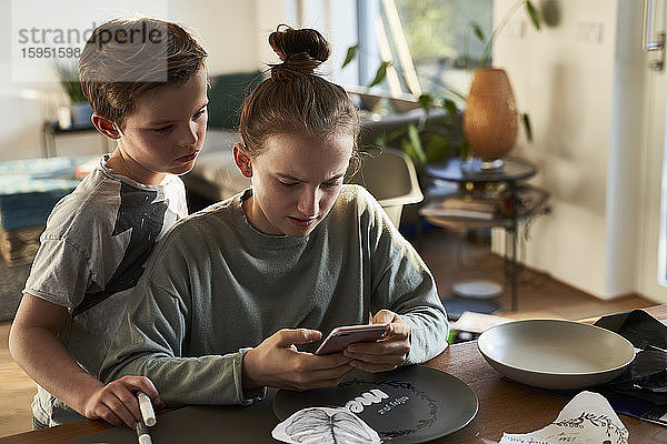 Bruder und Schwester zu Hause nutzen Smartphone für ein kreatives Online-Tutorial