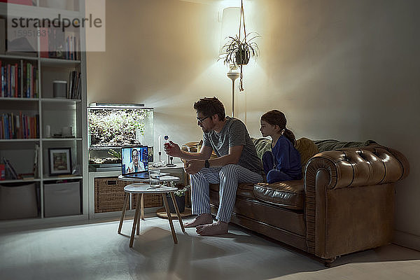 Krankes Mädchen sitzt neben dem Vater und diskutiert mit dem Arzt über Videoanruf per Laptop im heimischen Wohnzimmer über Telemedizin