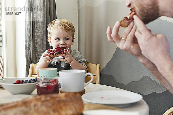 Porträt eines kleinen Jungen  der Brot mit Marmelade isst und seinen Vater beobachtet