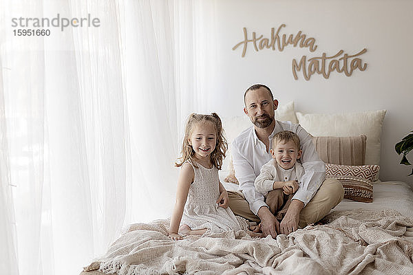 Familienporträt eines glücklichen Vaters und seiner zwei Kinder  die zusammen auf dem Bett sitzen