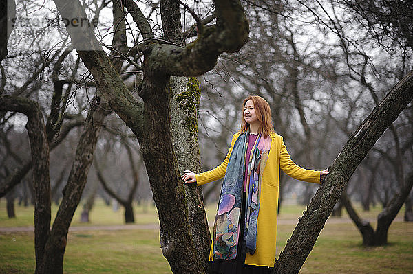 Lächelnde  nachdenkliche Frau balanciert auf kahlem Baum im Park