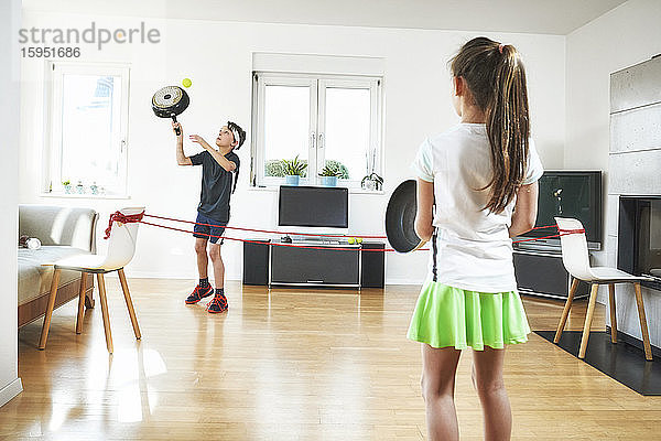Bruder und Schwester spielen während der Quarantäne zu Hause im Wohnzimmer Tennis