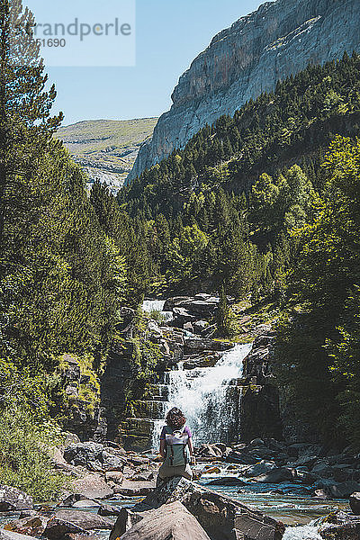 Spanien  Provinz Huesca  Wanderin bewundert kleinen Wasserfall am klaren Bergfluss