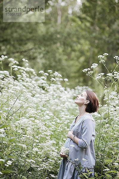 Schwangere Frau mit Händen auf dem Bauch entspannt sich inmitten von Blumen im Park