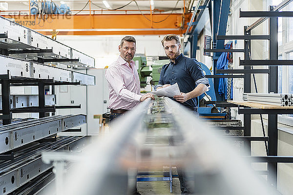 Zwei Männer untersuchen ein Stück Metall in einer Fabrik