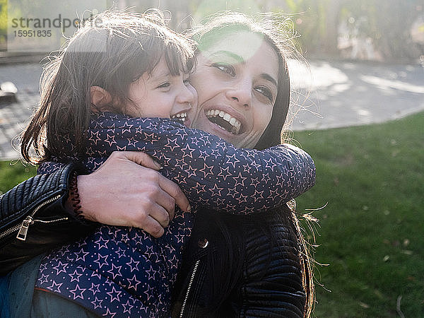 Porträt eines glücklichen kleinen Mädchens  das seine Mutter im Freien umarmt
