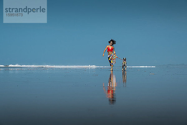 Unbeschwerte junge Frau geht mit ihrem Hund am Strand spazieren  Costa Rica