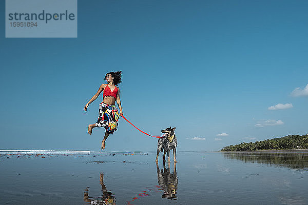 Unbeschwerte junge Frau geht mit ihrem Hund am Strand spazieren  Costa Rica