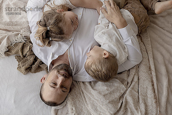 Porträt eines Vaters  der mit seinen beiden Kindern auf dem Bett liegt und sich entspannt