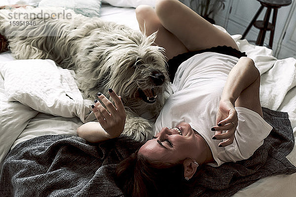 Reife Frau liegt auf dem Bett und spielt mit ihrem Hund