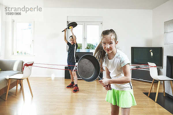 Lächelnde Schwester spielt Tennis mit Bruder zu Hause in Quarantäne