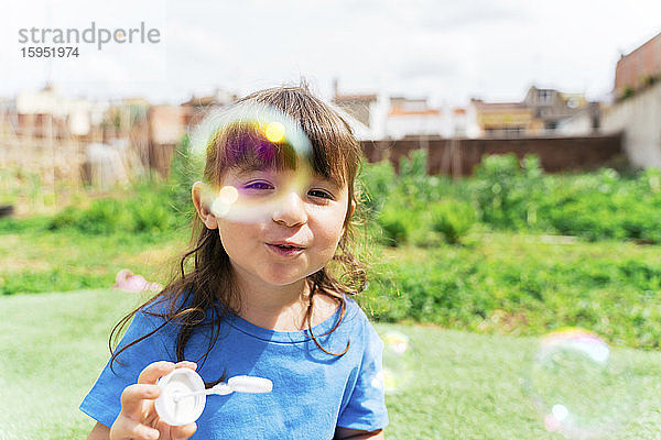 Porträt eines glücklichen kleinen Mädchens  das in einem Park Seifenblasen bläst