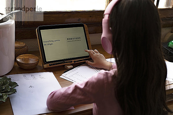 Mädchen mit Kopfhörern übersetzt Sprachen auf digitalem Tablet  während sie zu Hause Comics lernt