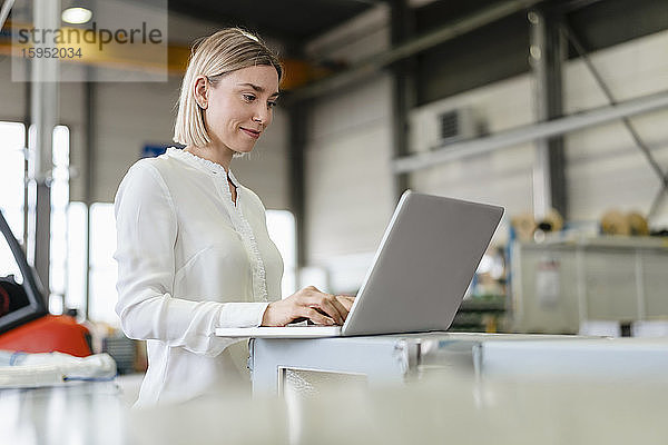 Lächelnde junge Frau mit Laptop in einer Fabrik