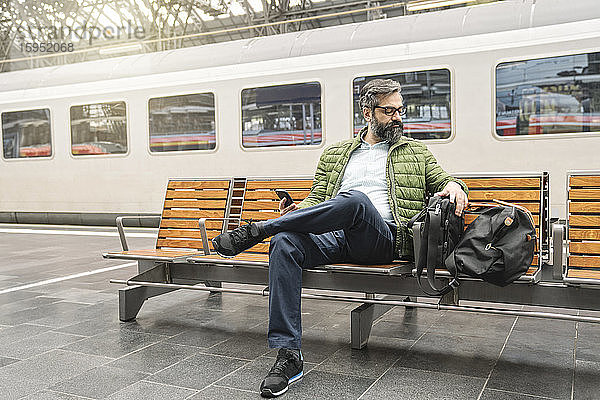 Mann sitzt auf einer Bank am Bahnhof