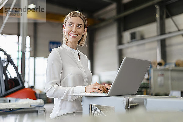 Lächelnde junge Frau mit Laptop in einer Fabrik