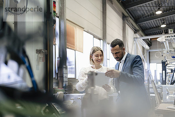Geschäftsmann und junge Frau mit Papieren im Gespräch an einer Maschine in einer Fabrik