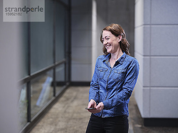 Lachende Geschäftsfrau benutzt Handy in moderner Büroetage