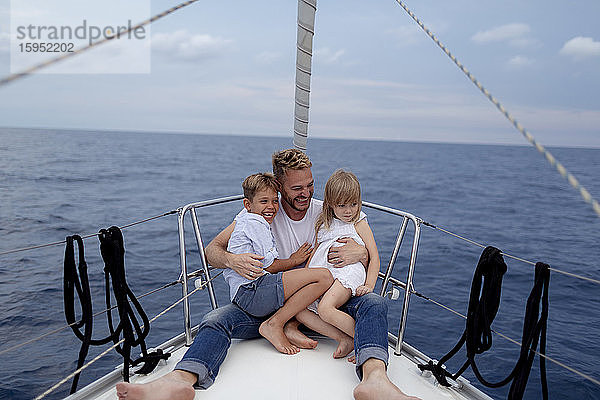 Vater mit seinen Kindern sitzt während der Segelfahrt auf dem Bootsdeck
