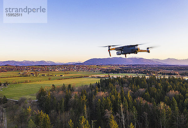 Deutschland  Bayern  Königsdorf  Drohne fliegt in der Dämmerung über ländliches Gehölz