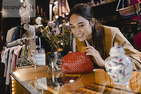 Lächelnder neugieriger Kunde mit Geldbörse betrachtet Vase im Secondhand-Laden