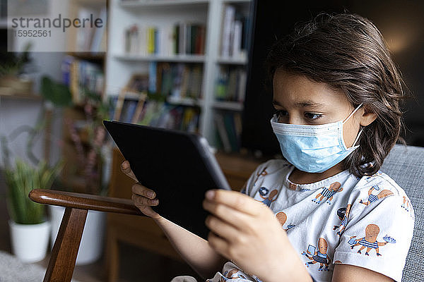 Junge mit chirurgischer Maske mit digitalem Tablett zu Hause