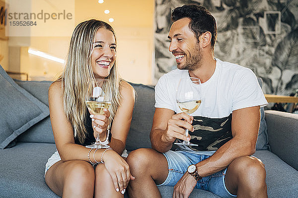 Porträt eines glücklichen Paares auf der Couch sitzend mit Weißweingläsern