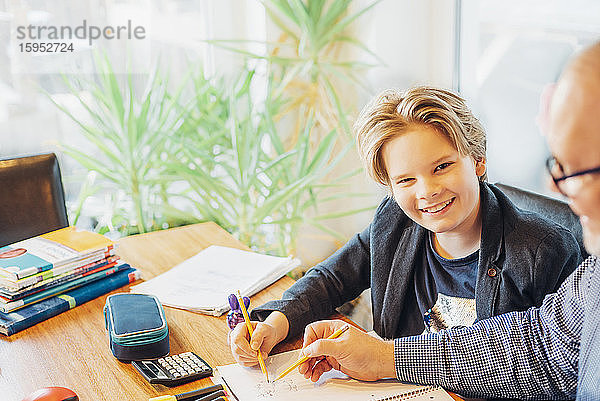 Porträt eines lächelnden Jungen mit einem Vater  der am Schreibtisch Hausaufgaben macht