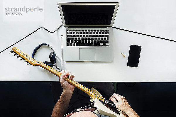 Draufsicht auf einen Mann  der mit einem Laptop online E-Gitarre lernt