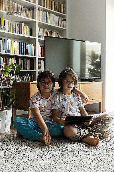 Porträt von zwei Brüdern mit digitalem Tablett auf dem Boden im Wohnzimmer sitzend