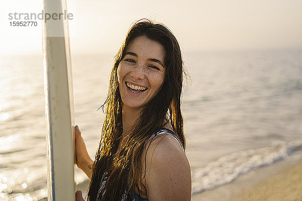Porträt einer lachenden jungen Frau mit Surfbrett am Strand  Almeria  Spanien