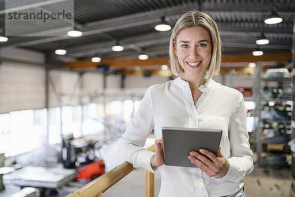Porträt einer lächelnden jungen Frau mit Tablette in einer Fabrik