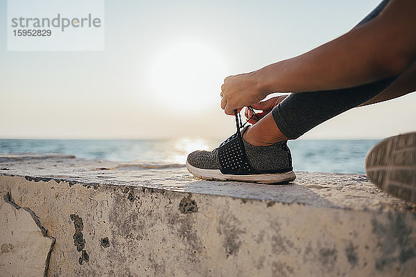 Unterer Abschnitt einer Sportlerin beim Schnürsenkelbinden auf der Promenade