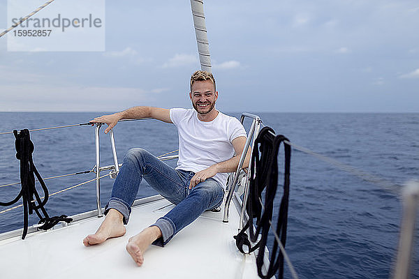 Lächelnder Mann sitzt während der Segelfahrt auf dem Bootsdeck