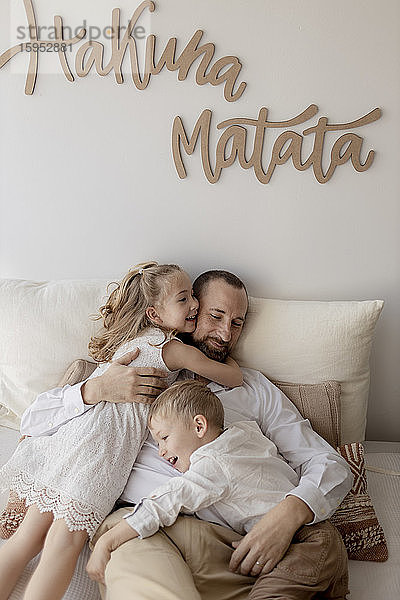 Familienporträt eines glücklichen Vaters und seiner zwei Kinder  die zu Hause kuscheln
