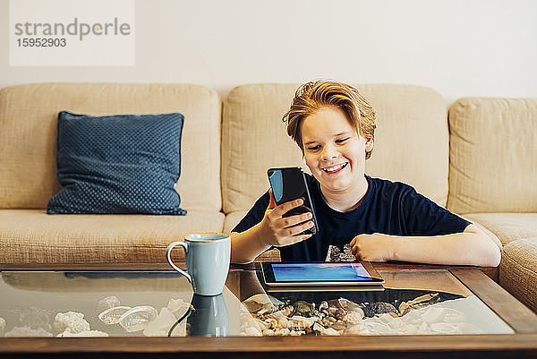 Glücklicher Junge benutzt Smartphone und Tablet im Wohnzimmer zu Hause