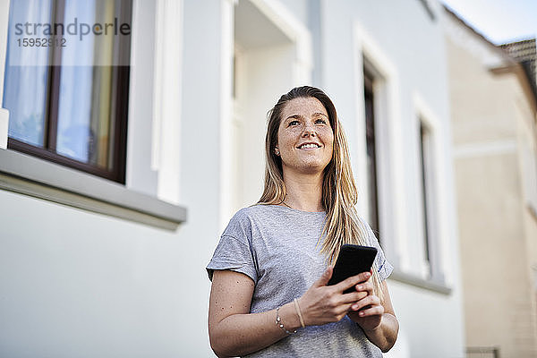 Frau schaut weg  während sie ihr Handy gegen das Haus hält