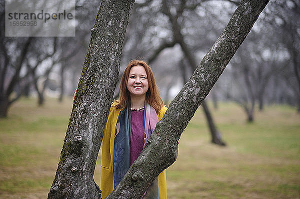 Porträt einer lächelnden Frau  die im Park an einem kahlen Baum steht