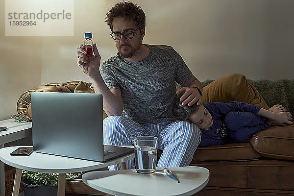 Mann bespricht Telemedizin mit Arzt über Videoanruf per Laptop  während er bei seiner kranken Tochter zu Hause im Wohnzimmer sitzt