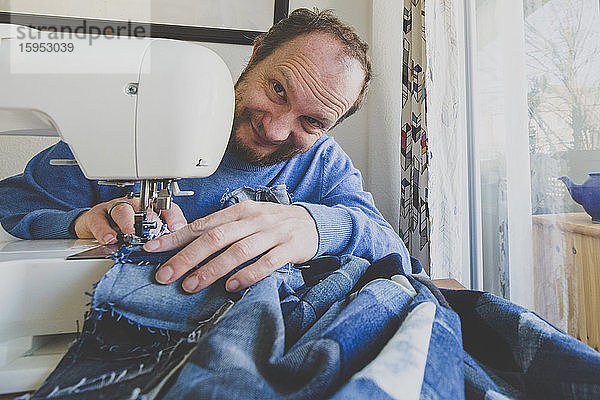 Porträt eines lächelnden Mannes  der zu Hause einen Jeansquilt näht