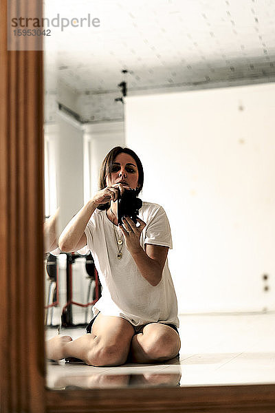 Spiegelbild einer reifen Frau  die auf dem Boden sitzt und mit der Kamera fotografiert