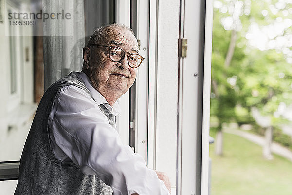 Porträt eines lächelnden älteren Mannes am offenen Fenster stehend