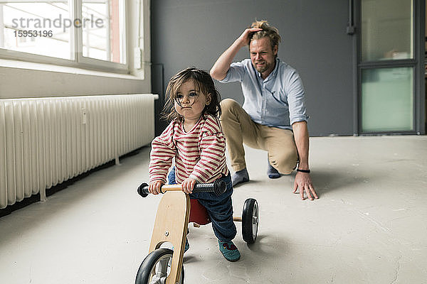 Lächelnder Vater beobachtet Tochter mit Balance-Fahrrad