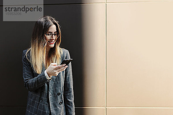 Lächelnde junge Geschäftsfrau schaut auf Handy