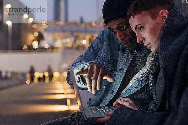 Glückliches junges Paar mit Laptop in der Stadt in der Abenddämmerung
