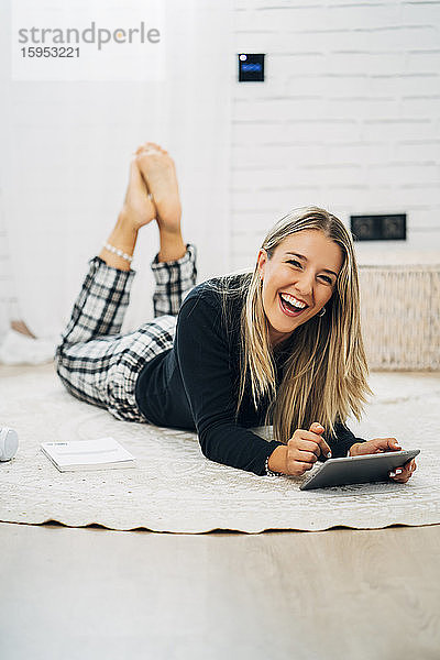 Porträt einer lachenden Frau  die mit einem Mini-Tablett auf dem Boden liegt