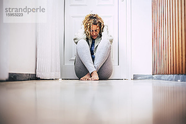 Verzweifelte Frau sitzt auf dem Boden im Flur vor verschlossener Tür