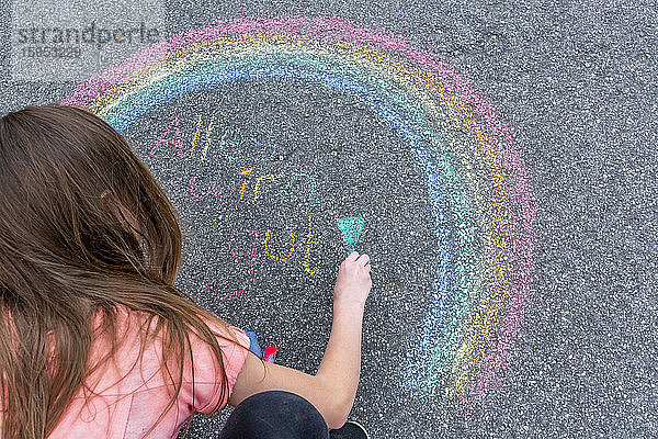 Mädchen malt Regenbogen auf Straße mit Text 'Alles wird sich fügen'