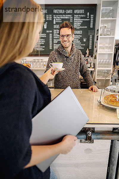 Junge Frau mit Laptop in einem Café  die eine Tasse Kaffee bestellt